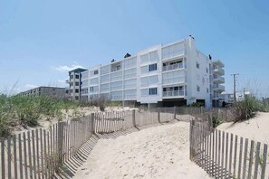 A multi-story hotel with a sandy beach path leading to the entrance, surrounded by wooden fences. - Direct oceanfront top floor condo w/outdoor pool, balcony, easy beach access (Ocean City)