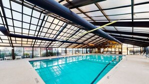 Una piscina interior con techo de cristal, agua cristalina y sillones blancos alrededor del borde.