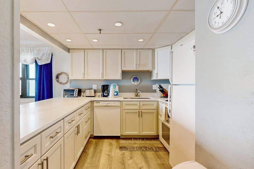 A compact kitchen with white cabinets, a dishwasher, a sink, and a clock on the wall.