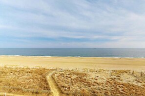 A beach with a sandy path leading to the water, a fence, and a distant ship. - Open & Spacious Condo w/Free WiFi, Central AC, Private W/D, Beachfront Location (Ocean City)
