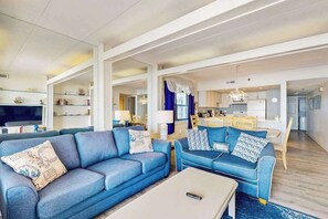 A modern living room with a blue sofa set, a coffee table, and a kitchen area in the background. - Open & Spacious Condo w/Free WiFi, Central AC, Private W/D, Beachfront Location (Ocean City)