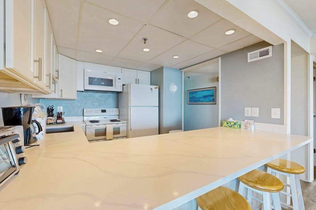 A modern kitchen with white cabinets, a central island, and bar stools.