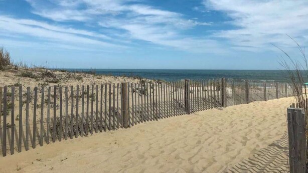 Una spiaggia sabbiosa con una recinzione in legno e cielo sereno.