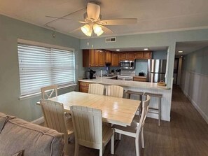 A kitchen with wooden cabinets, a dining table with chairs, a ceiling fan, and a refrigerator. - Diamond Beach 204 (Ocean City)