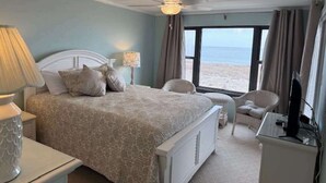 Una camera da letto con un letto, comodini, una sedia, una TV e vista sulla spiaggia.
