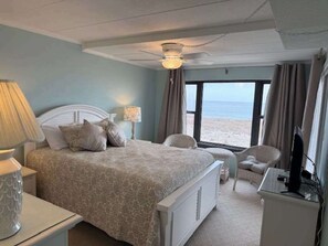 A bedroom with a bed, bedside tables, a chair, a TV, and a view of the beach. - Diamond Beach 204 (Ocean City)