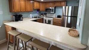 Una cucina con mobili in legno, un frigorifero in acciaio inox, un forno a microonde e un piano cottura. Ci sono due sgabelli al bancone.