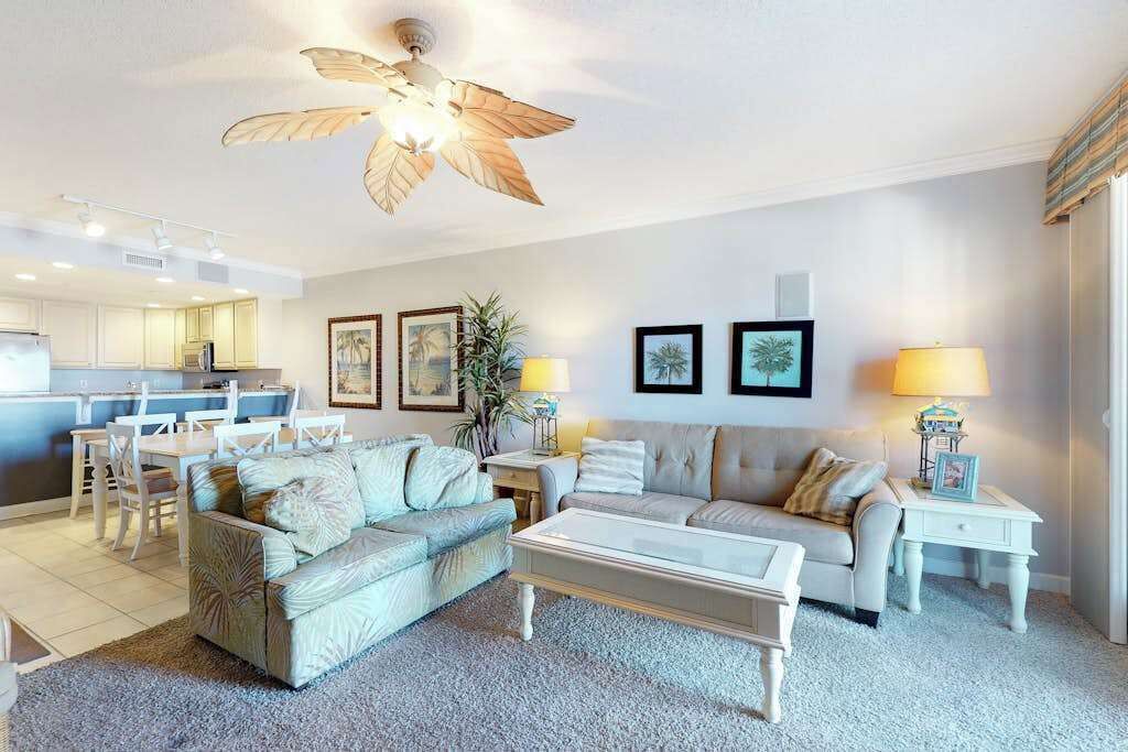 A spacious living room with a ceiling fan, a dining area, and a kitchen in the background.