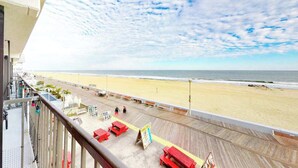 Uitzicht op een strand vanaf een balkon met een houten terras, rode banken en een bord.