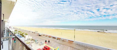 A beach view from a balcony with a wooden deck, red benches, and a signboard.