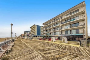 Eine Promenarde mit Bänken, ein Strand und ein mehrstöckiges Gebäude mit Balkonen.