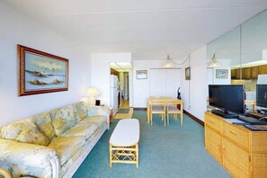 Ein Wohnzimmer mit Sofa, Esstisch, Fernseher und Küchenzeile.