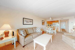 A living room with a sofa, coffee table, and dining area with chairs. - Vacation Retreat in Oceanfront Complex w/Free WiFi, Central AC, W/D (Ocean City)