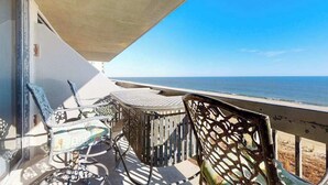 A balcony with outdoor furniture, a view of the sea, and a clear sky.