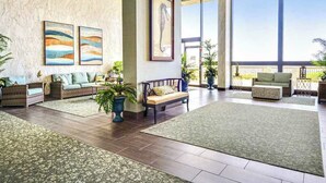 A spacious lobby with a high ceiling, large windows, and a seating area with wicker furniture.