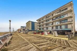 Eine Promenade mit Bänken, einem Restaurant direkt am Strand und mehrstöckigen Gebäuden mit Balkonen.