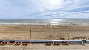 En utsikt över stranden från en terrass med ett räcke, en bänk och en soptunna.