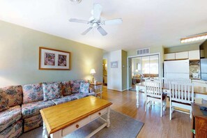 Ein Wohnzimmer mit Sofa, Couchtisch, Esstisch mit Stühlen, Deckenventilator und Küchenzeile.