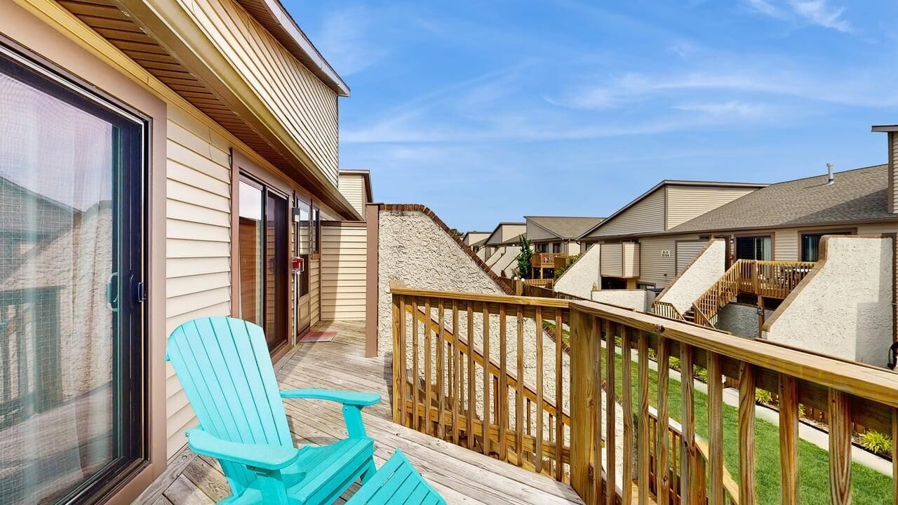 A residential building with a balcony, a sliding glass door, and a wooden deck.