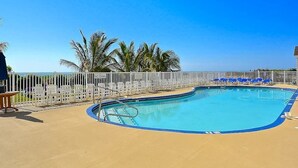Ein Pool mit weißem Zaun, blauen Liegestühlen und Palmen.
