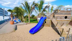 Ein Strand mit einer blauen Rutsche, Palmen und einer Holzkonstruktion.