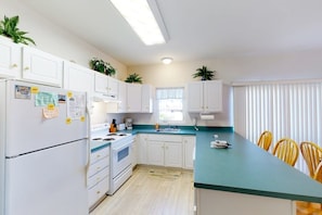 A kitchen with white cabinets, a stove, a sink, and a dining area with chairs. - Spacious Bayside Townhouse w/Deck, Balcony, Washer/Dryer, Central A/C, Free WiFi (Ocean City)