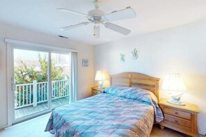 A bedroom with a bed, two bedside tables with lamps, a ceiling fan, a balcony with a white railing, and a view of trees and buildings. - Spacious Bayside Townhouse w/Deck, Balcony, Washer/Dryer, Central A/C, Free WiFi (Ocean City)