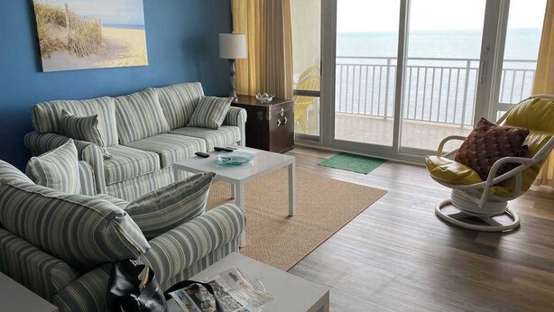 Ein Wohnzimmer mit einem gestreiften Sofa, einem kleinen Tisch, einem Sessel und Meerblick durch große Fenster.