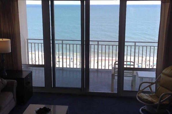 Ein Zimmer mit einer großen Schiebeglasdoor zum Balkon mit Blick auf Strand und Meer.