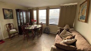 Ein Wohnzimmer mit Esstisch, Stühlen, einer Couch, einem Ventilator und großen Fenstern mit Blick.