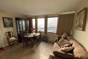 Ein Wohnzimmer mit Esstisch, Stühlen, einer Couch, einem Ventilator und großen Fenstern mit Blick.