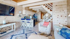 Un interior moderno con techo de madera, una zona de cocina, un área de estar con sofá y sillón, y una escalera.