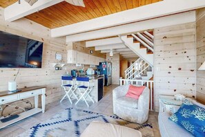 Ein modernes Interieur mit Holzboden, einer Küchenzeile, einer Sitzecke mit Sofa und Sessel sowie einer Treppe.
