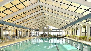An indoor swimming pool with a glass ceiling, lounge chairs, and potted plants. - Unique Condo w/Side Views of the Beach, Private Balcony, Shared Pools, Gym, A/C (Ocean City)