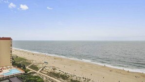 A beach view with a hotel building, a swimming pool, and a fence along the beach. - Unique Condo w/Side Views of the Beach, Private Balcony, Shared Pools, Gym, A/C (Ocean City)