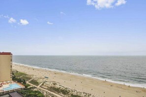 A beach view with a hotel building, a swimming pool, and a fence along the beach. - Unique Condo w/Side Views of the Beach, Private Balcony, Shared Pools, Gym, A/C (Ocean City)
