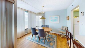 A dining area with a round table, chairs, a rug, and a ceiling light. - Unique Condo w/Side Views of the Beach, Private Balcony, Shared Pools, Gym, A/C (Ocean City)
