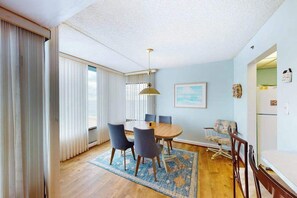 A dining area with a round table, chairs, a rug, and a ceiling light. - Unique Condo w/Side Views of the Beach, Private Balcony, Shared Pools, Gym, A/C (Ocean City)
