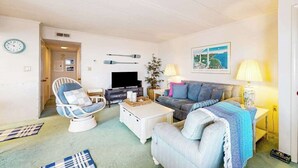 Una sala de estar con televisión, sofá, sillón y lámpara.