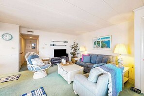 Ein Wohnzimmer mit Fernseher, einer Couch, einem Sessel und einer Lampe.
