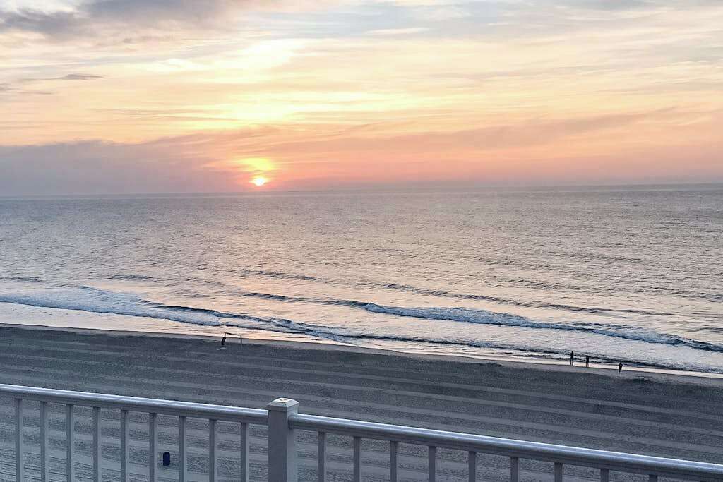 A beach with a sunset, waves, and a railing.