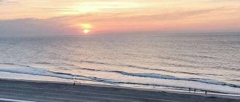 A beach with a sunset, waves, and a railing.