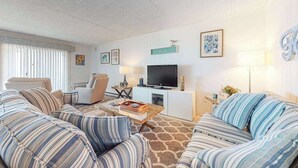 Een woonkamer met gestreepte banken, een flatscreen televisie, een salontafel en een tv-meubel.