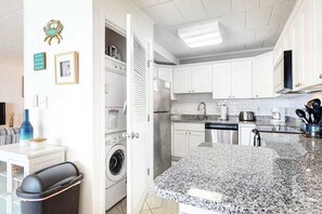 A kitchen with white cabinets, a granite countertop, a washing machine, and a dining area with a table and chairs. - Comfortable and Convenient Oceanside Condo w/Shared Pool, Free WiFi, & Balcony (Ocean City)