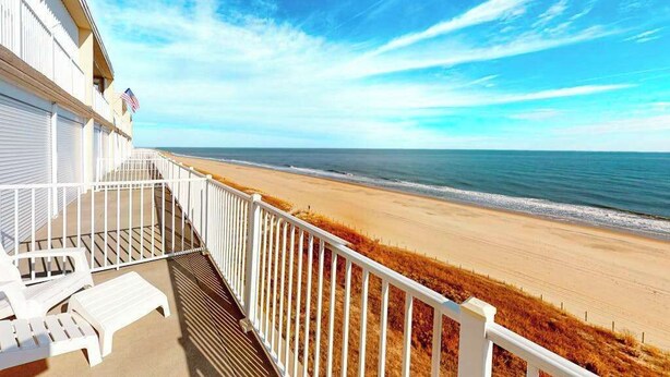 Een balkon met witte hekwerk en uitzicht op een strand.