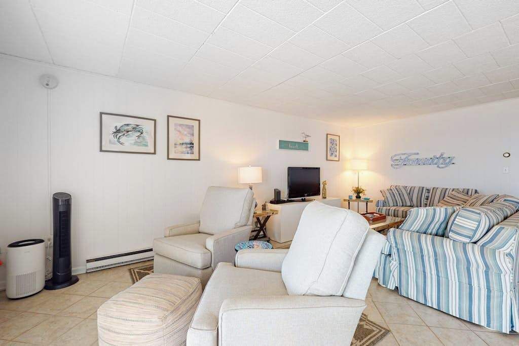 A living room with a sofa, armchairs, a television, and framed artwork on the wall.