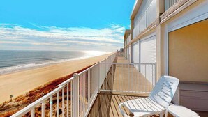 Een balkon met uitzicht op het strand, witte stoelen en een hekwerk.