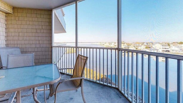 Ein Balkon mit Glastisch und -stühlen, Blick auf ein Gewässer und eine Ziegelmauer.
