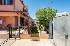Un vialetto stretto con un piccolo giardino, un cancello in metallo e un edificio con un balcone.