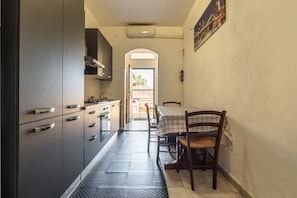 A narrow kitchen with a dining table and chairs, a view to the outside, and a fire extinguisher on the wall. - Casa Liliana – Maddalena Spiaggia: Bright Holiday Home Steps from the Sea (La Maddalena)